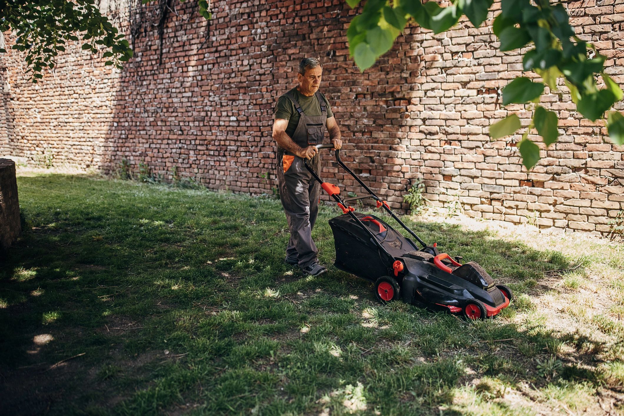 Senior man mowing a lawn in a backyard